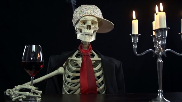 Beautiful shot of skeleton sitting at the table with glass of wine and cigarette