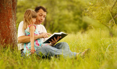 young father with his little daughter reads the Bible