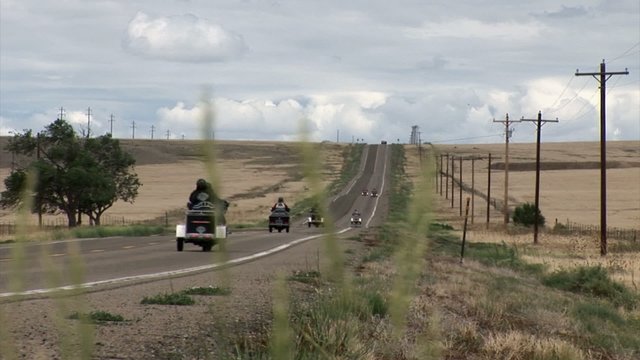Cars and motocycles are driving along the long prairie road