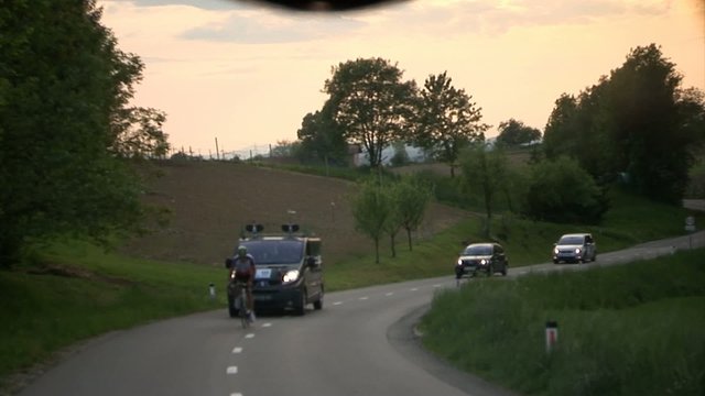 Shot through rear glass onto the country road and competing cyclists. Cyclists race across a small Eastern European country called Slovenia.
