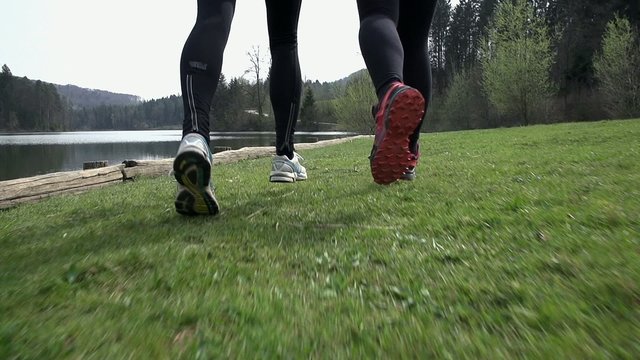 Low Angle Slow Motion Following Two Joggers Running On Grass