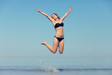 Beautiful young girl jumping on sea