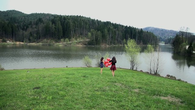 Two Female Friends With Red Balloons At Beautiful Lake