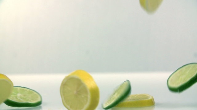 Pieces of lime and lemon falling in white background