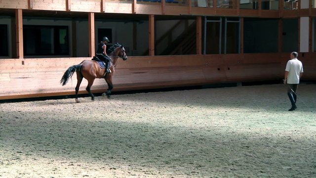 Big training place with young jockey girl riding horse trained by male trainer