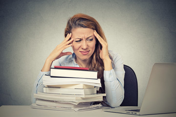 stressed woman sitting at desk with books computer