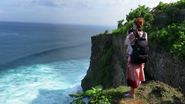 Woman standing on cliff's edge in Uluwatu and taking photos