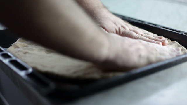 Close up shot of a black baking sheet and man is putting on dough and arranging it around the baking sheet