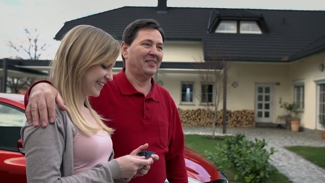 Father and his daughter stand by red car and wave to the man leaving