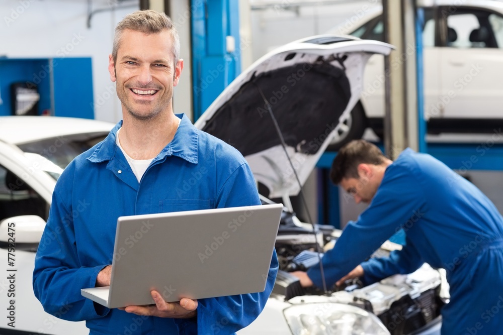 Poster smiling mechanic using a laptop