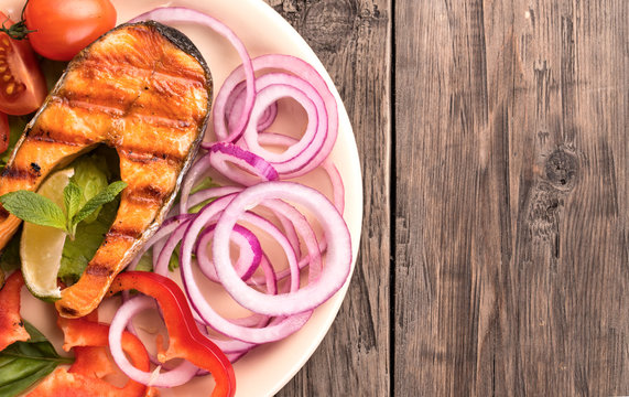 Grilled salmon steak with sliced onion and tomatoes at left