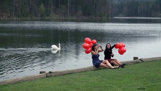 Female Friends Enjoying With Red Balloons And Swan in Lake
