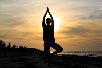 Silhouette of young man doing yoga at sunset