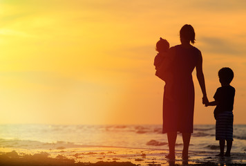 mother and two kids walking on beach at sunset