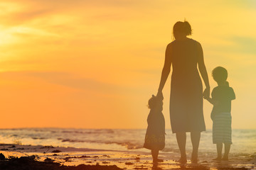 mother and two kids walking on beach at sunset