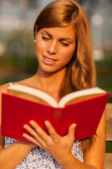brunette woman is reading a book on a bench