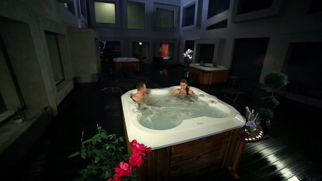young couple relaxed in jacuzzi with roses and champagne in the front   