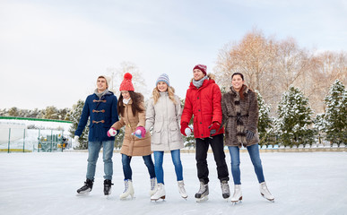 happy friends ice skating on rink outdoors