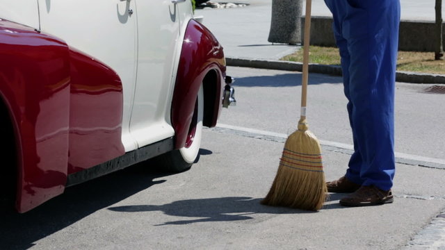 Sweeping a parking lot with a brom and vintage car