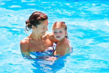 Happy mother and baby daughter swimming pool