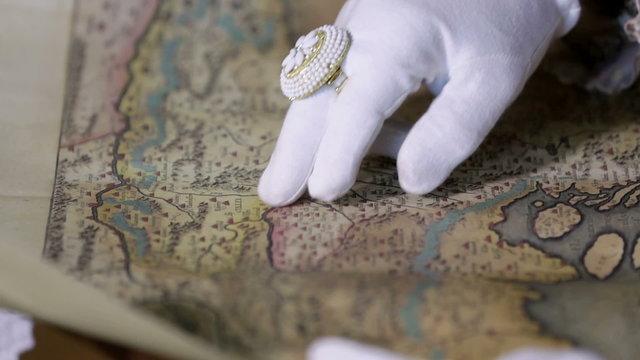 Man with white gloves is reading an old geographical map