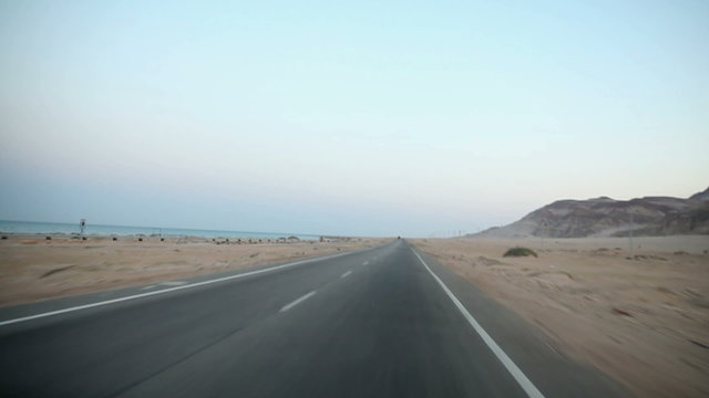 Driving on empty road by the sea in desert