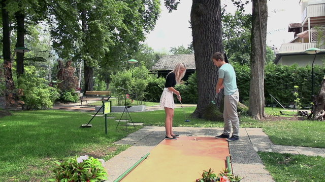 Boyfriend teaching girl playing miniature golf in slow motion