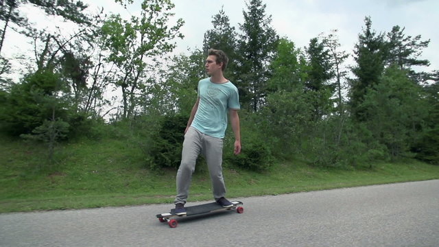 Young longboarder skating down the road in slow motion
