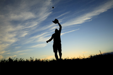 A man silhouetted by the sunset is just beginning catch ball