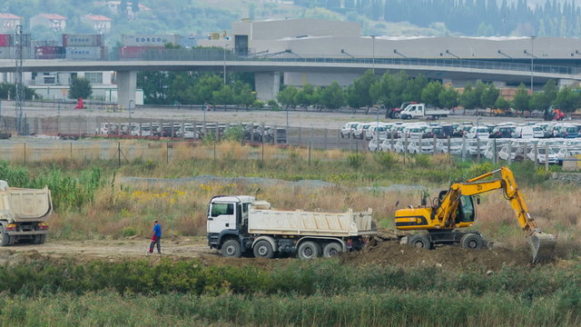 KOPER, SLOVENIA - SEP 15, 2013: Excavator is loading big white truck with soil