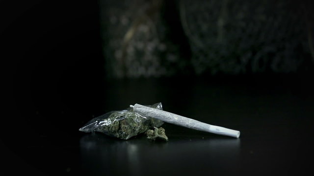 Joint falls on a pack of marihuana on the black background in slo-mo