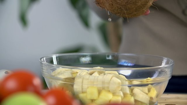 Pouring coconut milk into the bowl with all kind of fruit
