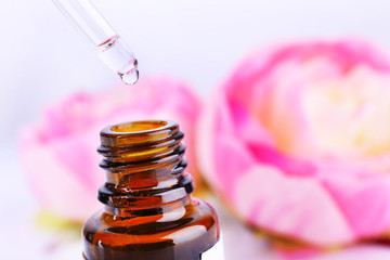 Dropper bottle of perfume with flowers on light background