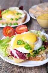 Toast with egg Benedict and tomato on plate on wooden table