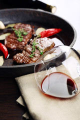 Glass of wine and steak in frying pan on table close up
