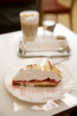 The piece of sweet cake on white table against glass of coffee