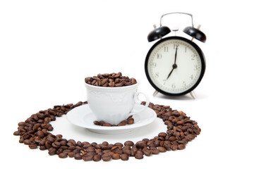 The porcelain cup filled by coffee beans and alarm clock