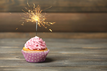 Cupcake with sparkler on table on wooden background