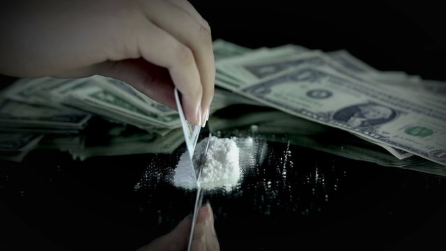 Female making some cocaine lines with credit card with money bills in the back
