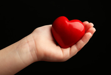 Obraz premium Heart in child hands on black background