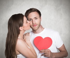 Fototapeta na wymiar Composite image of woman kissing man as he holds heart