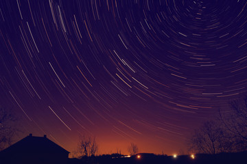 Star trails around Polar star with distant city glow.