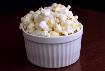 Popcorn in a white ceramic bowl over wood background