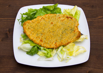 Breaded cutlet with salad on wooden table on