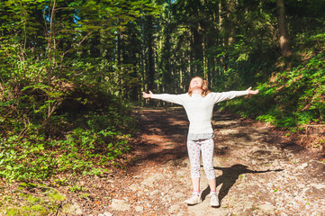 Kid girl with arms open wide, standing in the middle of forest