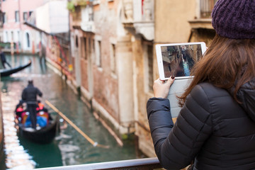 Fototapeta na wymiar Young girl using a tablet to take pictures of gondolas of Venice