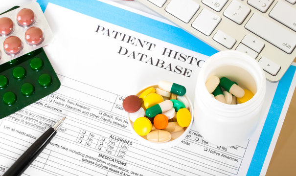 Doctor workplace. Pills, tablets, pen on patient history databas