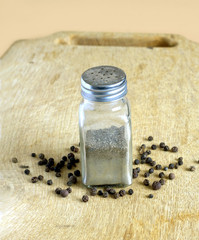 Glass jar with black pepper peas on a wooden chopping board