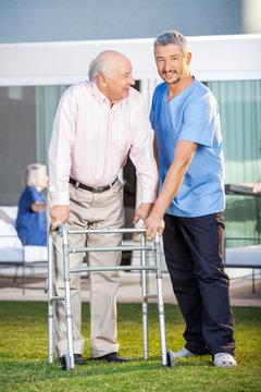 Smiling Caretaker Assisting Senior Man To Use Walking Frame