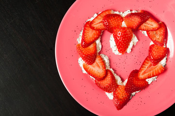 heart shaped strawberry in a pink plate on black background